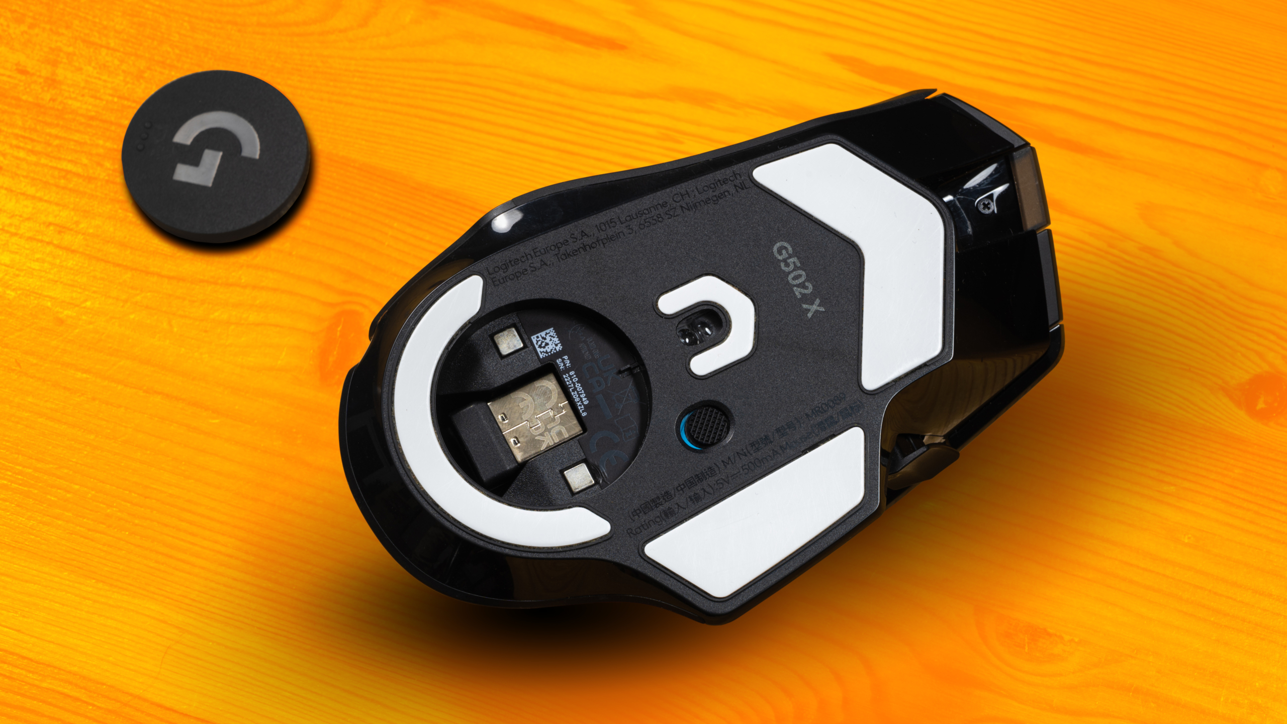 Onderzijde van de G502X-muis van Logitech, met onderop PTFE-glijvoetjes en een uitsparing voor zowel de USB-dongle als een PowerPlay-puck in plaats kan nemen.