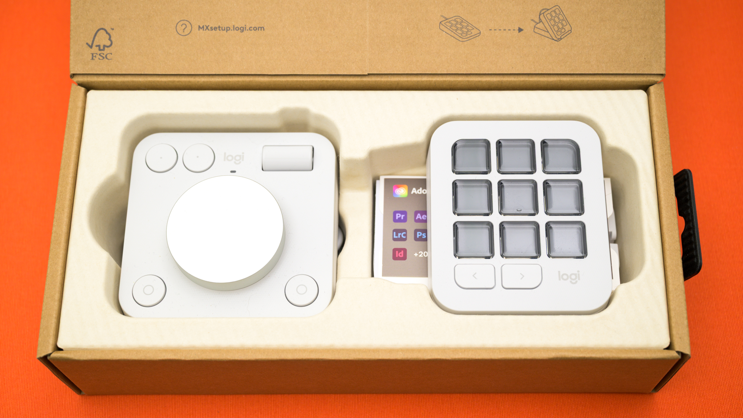 Bovenaanzicht van de Logitech MX Creative Console in de doos. Links de Dialpad, rechts de Keypad, met daaronder een tegoedkaart voor drie maanden Adobe Creative Cloud.