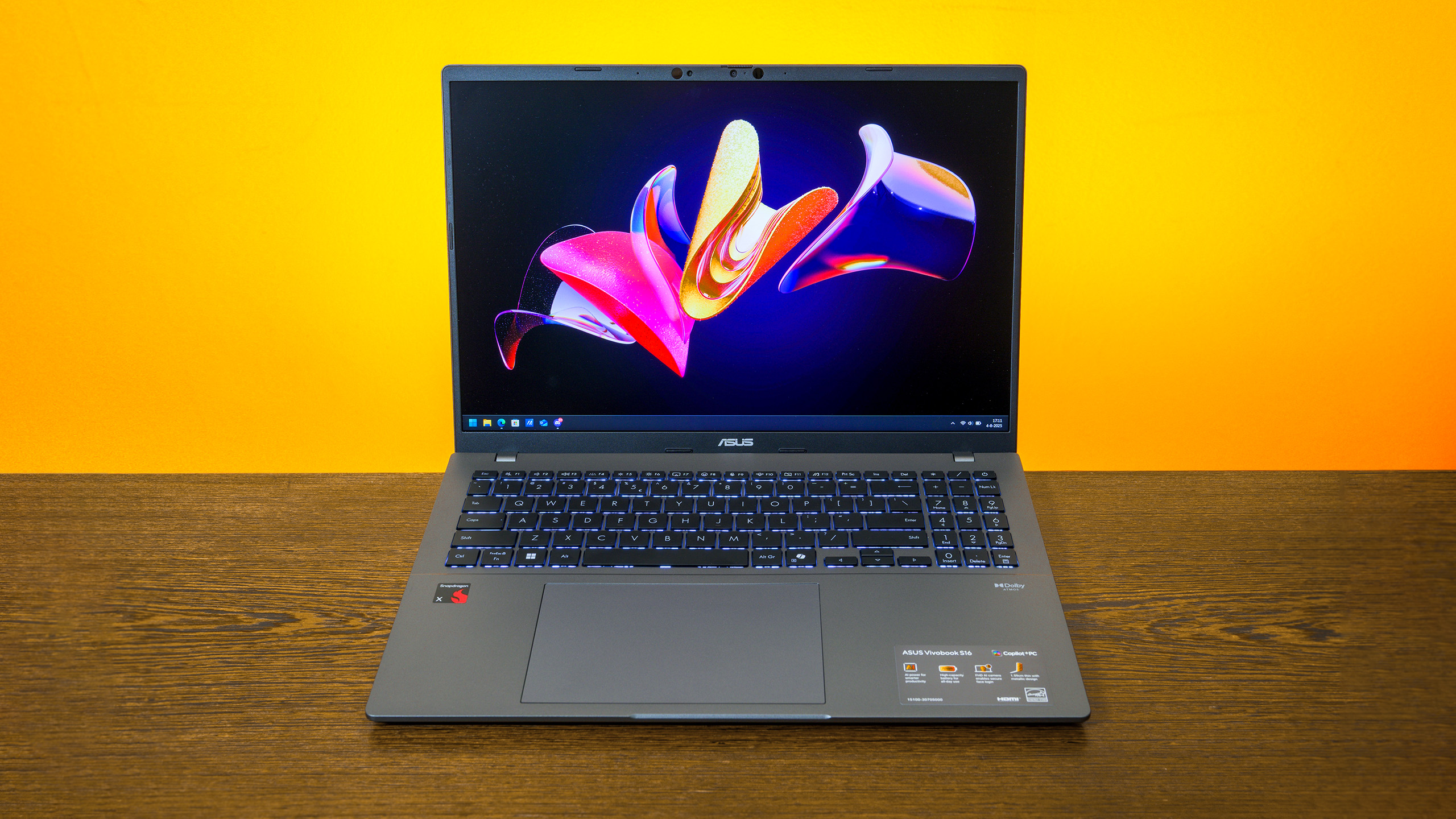 Vooraanzicht van ASUS' Vivobook 16, met Snapdragon X-chip, opengeklapt op een tafel. Op het scherm staat een Windows 11-bureaublad afgebeeld.