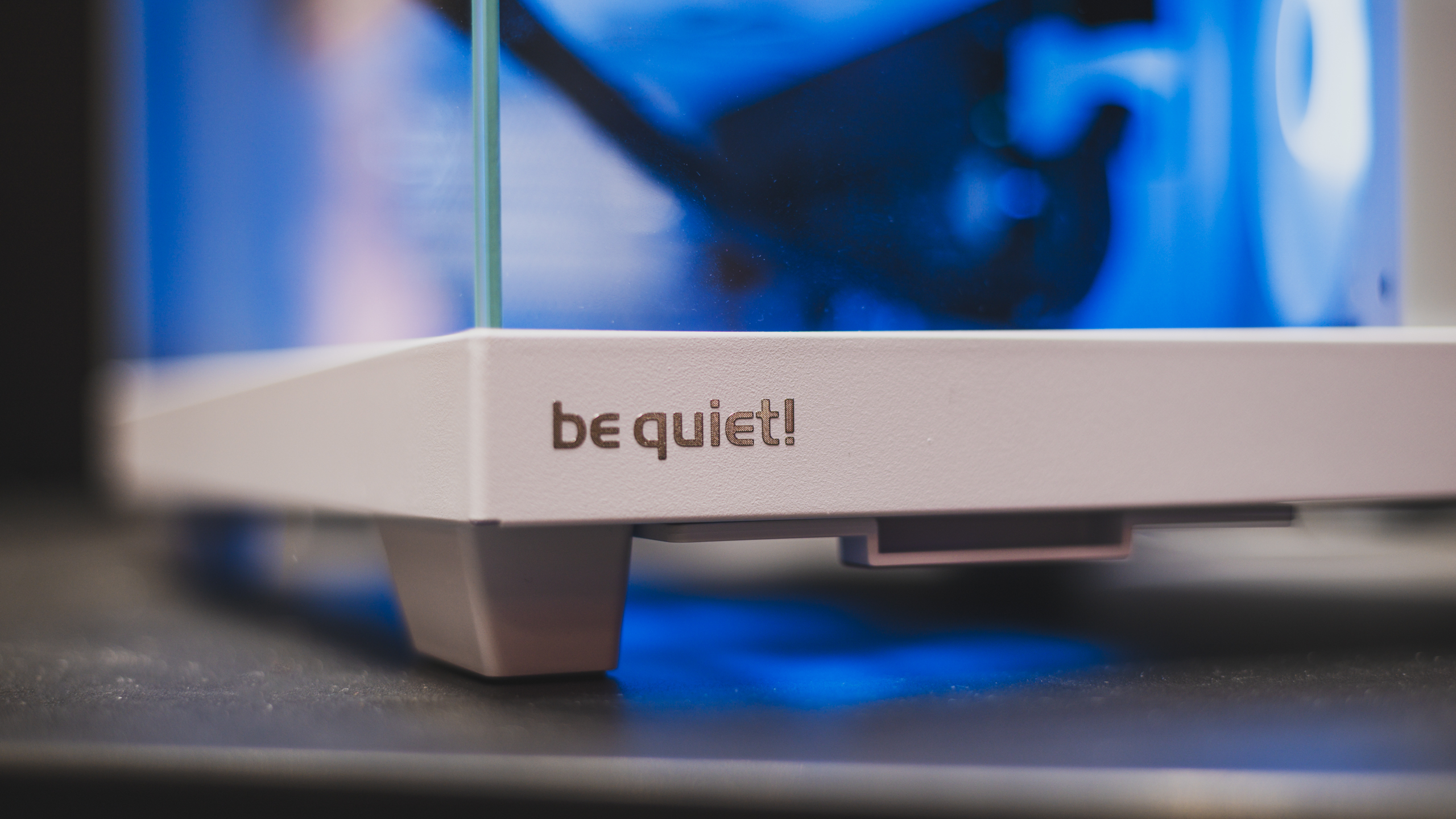 Close-up van de voorzijde van de witte uitvoering van be quiet! Light Base 500 LX, met het logo prominent in beeld. Daarachter: veel blauwe RGB-verlichting.