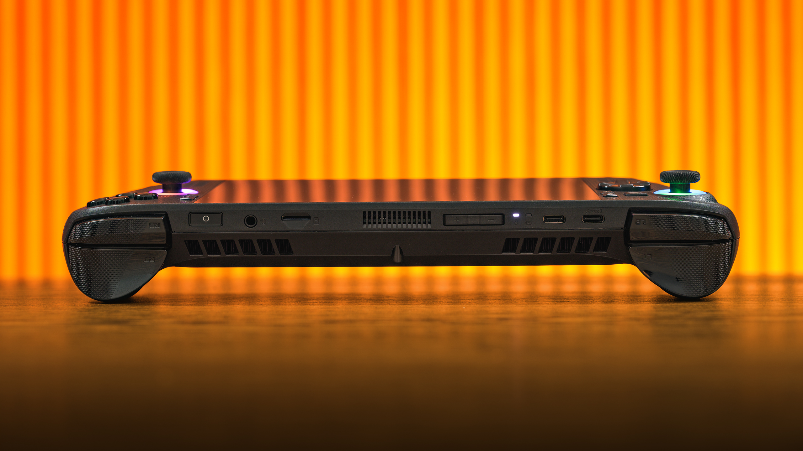 De ROG Xbox Ally X ligt plat op een bureaublad, bekeken van de bovenkant van het apparaat. Zichtbaar zijn de vingerafdrukscanner, microSD-kaartlezer, volumebesturing, audio-jack, twee USB-C-poorten en een reeks ventilatieroosters.