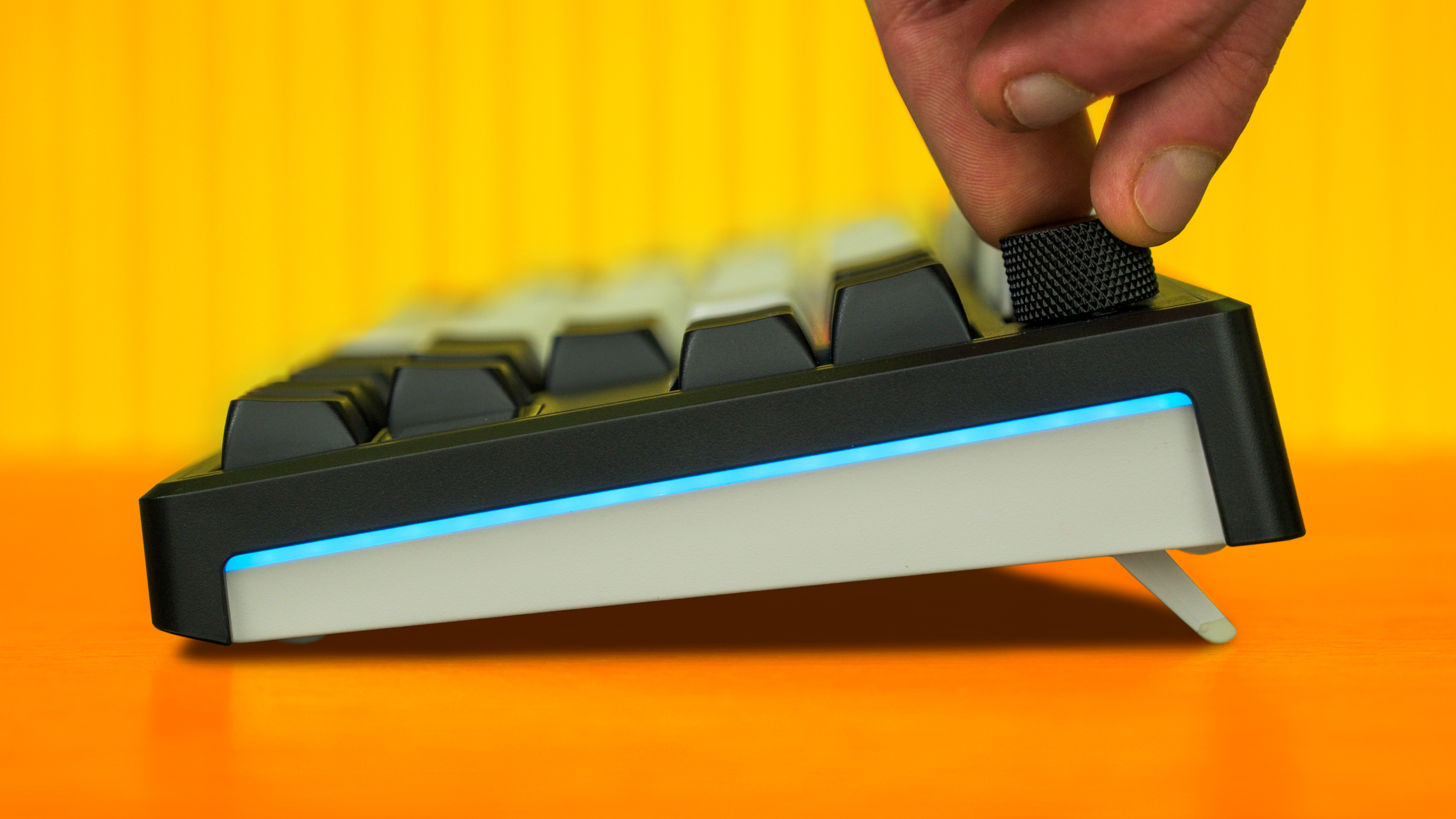 Profielaanzicht van de Hator Skyfall 80 MAG Ultima 8K. Een hand friemelt aan het 'control knob'-scrollwieltje en de RGB-gloed op de zijkant van het toetsenbord is goed zichtbaar.